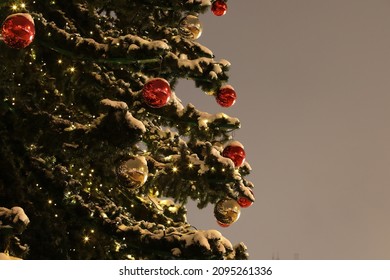 Christmas Tree With Snow Decorated With Festive Balls And Glowing Lights Standing Outside Isolated On Gray