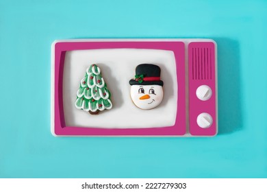 A Christmas tree and a snowman on the white screen of a retro tv with magenta frame against blue background. Surreal concept for romantic Christmas movies on television in winter time.