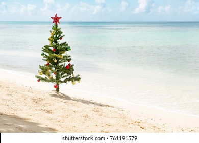 Christmas tree with star on top and baubles standing by a sunny beach - Powered by Shutterstock