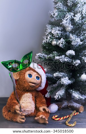 Christmas tree, a symbol of the new year 2016 a toy monkey in a red cap of Santa Claus and the brilliant green half mask in his hand on the wooden floor, there is an empty space for text greetings
