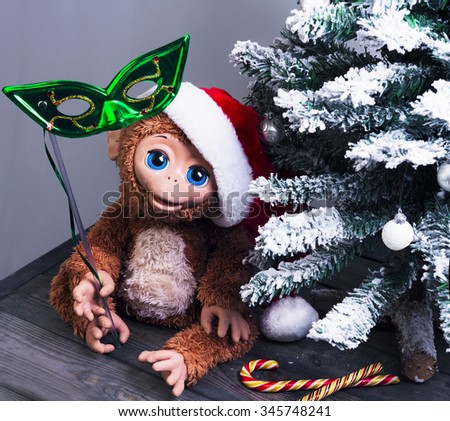 Christmas tree, a symbol of the new year 2016 a toy monkey in a red cap of Santa Claus and the brilliant green half mask in his hand on the wooden floor, there is an empty space for text greetings