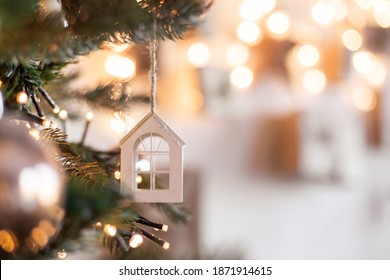 Christmas Tree Toy In The Form Of A House On A Branch. Christmas Mood Background. Vacation Atmosphere. Comfort Hyuge Concept Cozy. Family Budget Mortgage Buying Real Estate