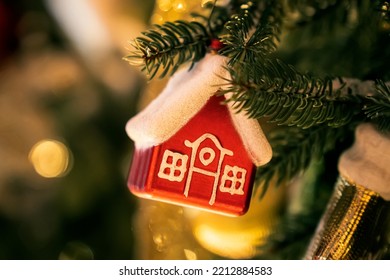 Christmas Tree Toy In Form Of A House On A Branch. Christmas Mood Background. Vacation Atmosphere. Chousing Rental Concept, Realtor Services, Mortgage, Purchase, Loan. Mortgage Buying Real Estate