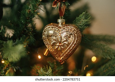 Christmas tree with vintage heart and baubles with golden lights close up. Modern decorated christmas tree branches with stylish ornaments in festive room. Winter holidays, atmospheric time