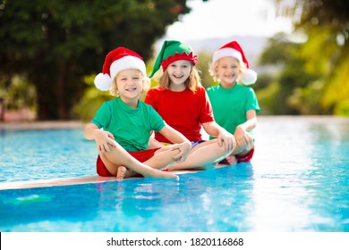 Christmas Vacation On Tropical Island. Kids In Santa Hat Playing In Swimming Pool On Family Xmas Vacation. Winter Holidays At The Beach. Travel With Children. Boy And Girl Swim. Merry Christmas Card.