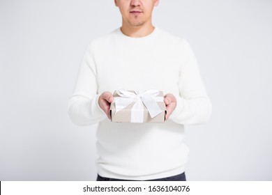 Christmas or Valentine's day concept - gift box with white ribbon in male hands over gray background with copy space