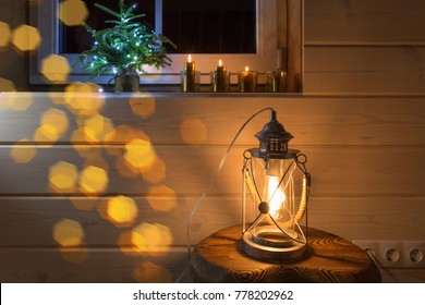 Christmas window decoration with four golden burning candles and a lantern for a background in wooden house. Advent candles and small christmas tree.