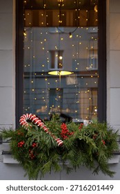 Christmas window display with pine branches, red berries, candy cane illuminated by warm interior lighting. Winter holiday window with evergreen greenery and festive candy cane, inviting seasonal mood