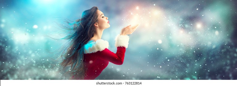 Christmas Winter Fashion Girl Blowing  Magic Snow In Her Hand. Fairy. Beautiful New Year And Xmas Tree. Holiday Hairstyle, Makeup. Gift. Beauty Model Woman On Holiday Blurred Blue Background, Sale