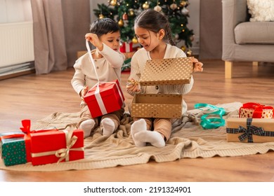 christmas, winter holidays and childhood concept - happy little girl and boy opening gifts sitting on floor at home - Powered by Shutterstock