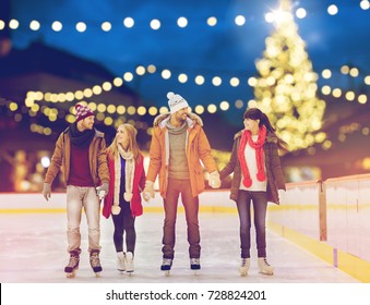 christmas, winter and leisure concept - happy friends holding hands on skating rink over outdoor holiday lights background