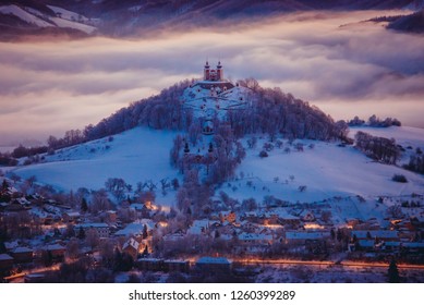 Christmas In Winter Old City. Banska Stiavnica, Slovakia. Church At The Top Of The Hill. Light Of Houses In The Valley