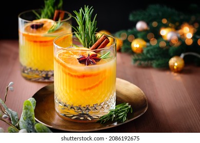 Christmas or winter warming bourbon old fashioned with oranges, cinnamon and rosemary on wooden table with tree branches and golden decor, top view - Powered by Shutterstock