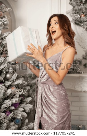 Christmas Winter Woman holding magic Christmas Gift box. Beautiful New Year and Christmas Tree. Beauty Fashion Model Girl With Present Box. Merry Christmas and Happy New Year
