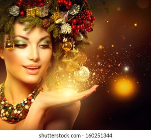 Christmas Winter Woman With Miracle In Her Hand. Fairy. Beautiful New Year And Christmas Tree Holiday Hairstyle And Makeup. Gift. Magic Girl. Beauty Fashion Model Over Holiday Blurred Background. 