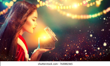 Christmas Winter Woman opening magic Christmas Gift box. Fairy. Beautiful New Year and Christmas scene, Beauty Fashion Model Girl With Present Box at night. Holiday Magic stars and light - Powered by Shutterstock