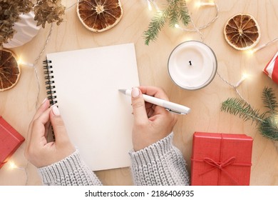 Christmas wish list writing. Woman creating present list for winter holidays. Top view, flat lay. Preparing for Xmas and New Year concept. Female hand writing in empty notebook on wooden table. - Powered by Shutterstock