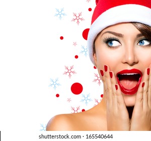 Christmas Woman. Beauty Model Girl In Santa Hat Isolated On White Background. Funny Laughing Surprised Woman Portrait. Open Mouth. True Emotions. Red Lips And Manicure. Beautiful Holiday Makeup. 