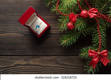 Christmas Wooden Background With Christmas Tree And Red Ornaments. Christmas Background With Red Wooden Box. A Christmas Gift. Gift On Valentine's Day. Jewelry Red Wooden Box. Ring With Blue Gem