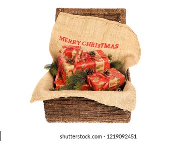 Christmas wrapped gifts with red ribbons on a jute sack with text "Merry Christmas", decorated with pine cones and pine twigs in an open wicker basket, isolated on white background  - Powered by Shutterstock