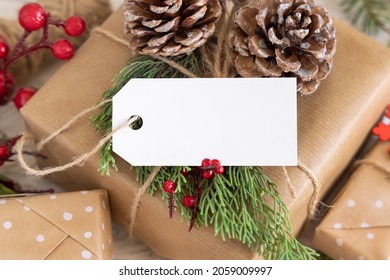 Christmas Wrapped Present With Paper Gift Tag With Fir Tree Branches, Pine Cones And Holiday Decorations Close Up. Rustic Winter Composition With Blank Gift Tag Mockup, Copy Space, Close Up