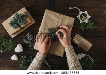 Christmas wrapping idea, xmas wrapping workspace. Female hands wrap gift box in kraft recycled paper. Eco-Friendly, Sustainable, zero waste, natural color Christmas gift boxes on wooden background