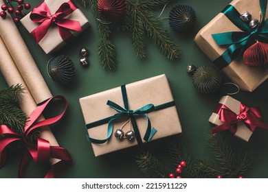 Christmas wrapping table with gift boxes, ribbons, paper rolls on dark green background.