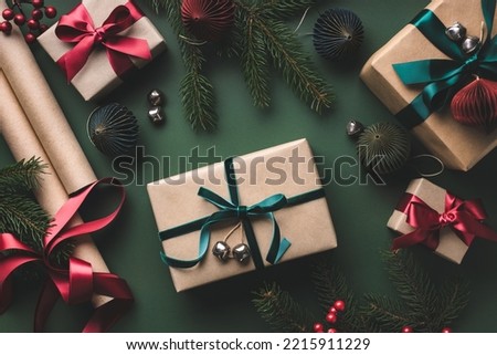 Christmas wrapping table with gift boxes, ribbons, paper rolls on dark green background.