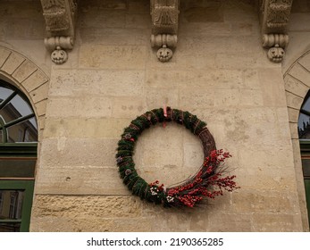 Christmas Wreath Decorated With Red Berries Hanging On The Beige Wall. Close Up View Of Christmas Decorations Outside During The Festive Period In Lviv. Big Wreath On The House.