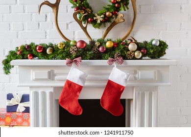 christmas wreath with decorations, stockings and deer horns over fireplace mantel - Powered by Shutterstock
