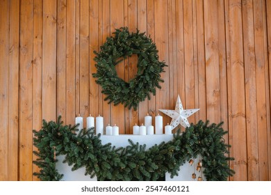 A Christmas wreath hangs above a mantel adorned with a garland of evergreen branches and candles. This cozy arrangement evokes a warm holiday atmosphere in a rustic room. - Powered by Shutterstock