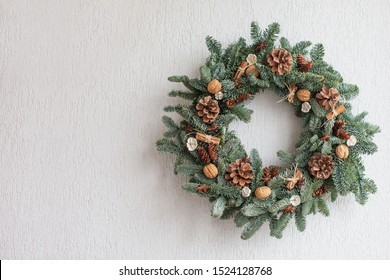 Christmas wreath made of natural fir branches  hanging on a white wall.  Wreath with natural ornaments: bumps, walnuts, cinnamon, cones. New year and winter holidays. Christmas decor. Copy space - Powered by Shutterstock