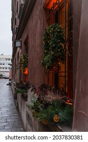 Christmas Wreath On A Restaurant Window. Beautiful Holiday House Is Decorated With Coniferous Wreaths And Small Garlands. Christmas Wreath With Christmas Trees And Garlands On Background Of Red House.