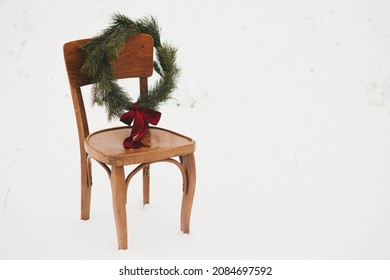 Christmas wreath on rustic chair in snowy winter field. Merry Christmas! Winter holidays in countryside. Space for text. Stylish xmas wreath with pine branches and red bow hanging on wooden chair - Powered by Shutterstock