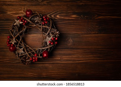Christmas wreath with red apples and berries on brown wooden background. Top view. Copy space