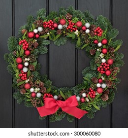 Christmas Wreath With Red Bow And Bauble Decorations, Holly, Mistletoe And Winter Greenery Over Dark Blue Oak Front Door Background.