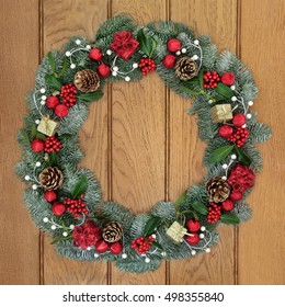 Christmas Wreath With Red And Gold Bauble And Gift Box Decorations, Holly, Mistletoe, Pine Cones And Snow Covered Blue Spruce Fir Over Oak Wood Front Door Background.