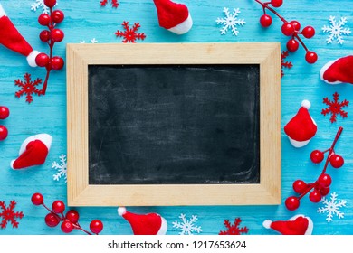 Christmas Xmas New Year holiday background - empty black chalkboard in wooden frame on blue background with festive decorations santa hat, snowflakes, decorative red berry - Powered by Shutterstock