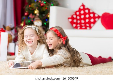 christmas, x-mas, winter, happiness concept - two adorable curly girls playing with tablet pc 