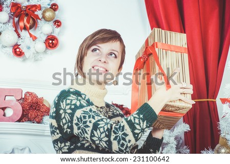 christmas, x-mas, winter, happiness concept - smiling young woman in green sweater with gold gift box near Christmas background 