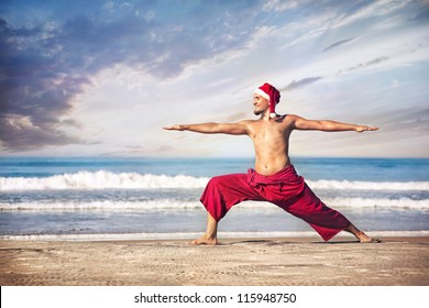 Christmas yoga warrior pose by man in red trousers and Christmas hat on the beach near the ocean in India