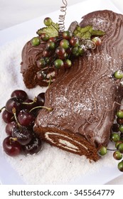 Christmas Yule Log, Buche De Noel, Chocolate Cake With Branch, Fresh Cherries And Festive Berry Decorations On A White Serving Platter, Overhead. 