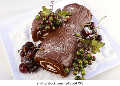 Christmas Yule Log, Buche De Noel, Chocolate Cake With Branch, Fresh Cherries And Festive Berry Decorations On A White Serving Platter, Overhead. 