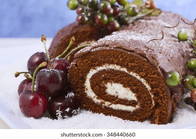 Christmas Yule Log, Buche de Noel, chocolate cake with branch, fresh cherries and festive berry decorations on a white serving platter, closeup. 