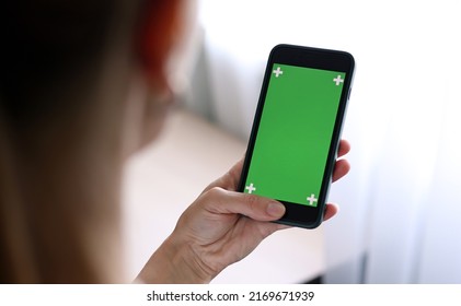 Chroma key mockup on smartphone in hand. Woman holds mobile phone iPhone and swipes photos or pictures left indoors of cozy home. Use green screen for copy space closeup - Powered by Shutterstock