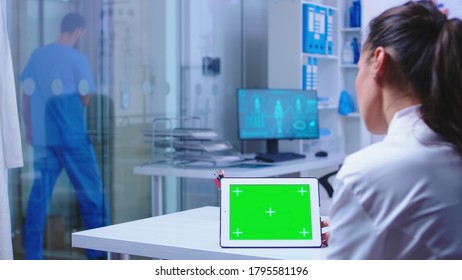 Chroma Key On Tablet Pc Display Used By Doctor In Hospital Cabinet And Nurse Leaving The Clinic Wearing Blue Uniform. Doctor In Health Clinic Working On Tablet Computer With Replaceable Screen Doing