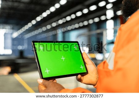 Chroma key screen on tablet with black supervisor next to machinery on factory floor. Worker showing engineering responsibilities and manpower behind steel fabrication and production.