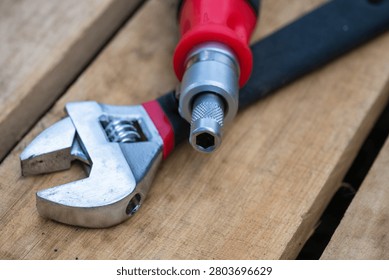 a chrome adjustable wrench and a red-handled multi-bit screwdriver resting on a textured wooden surface.