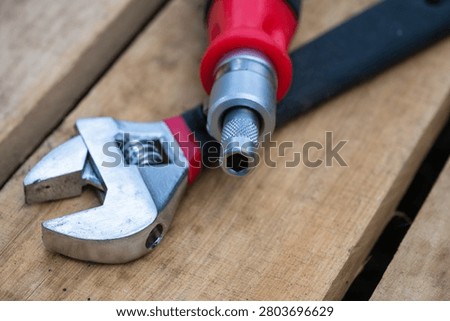 a chrome adjustable wrench and a red-handled multi-bit screwdriver resting on a textured wooden surface.