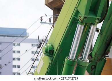 Chrome Hydraulic Cylinder Of Green Crane With Building As Background.